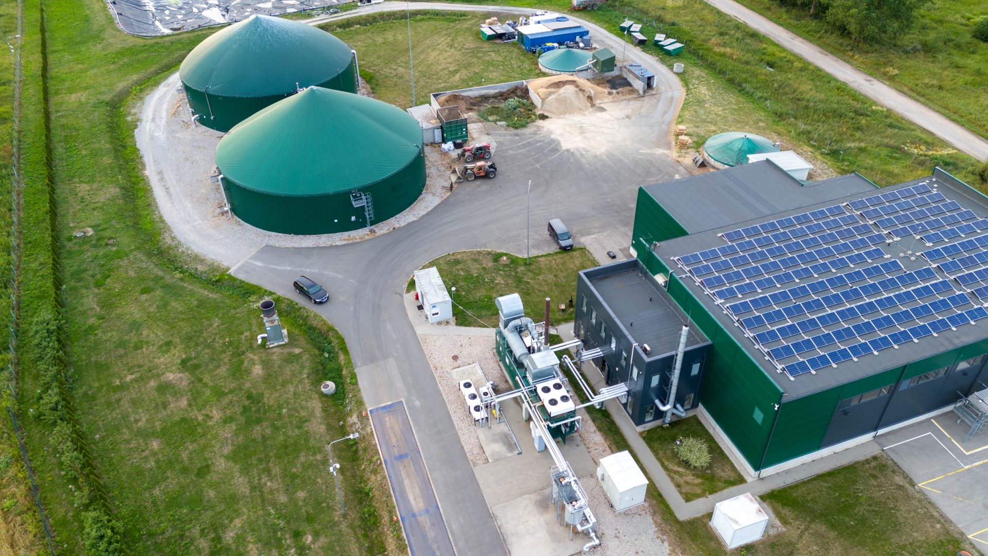 Biogas Aerial view of a biogas plant with large green digesters, a processing facility equipped with rooftop solar panels, and various infrastructure for renewable energy production.